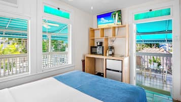 A hotel room with a bed, a desk with a TV, and a balcony with a view.