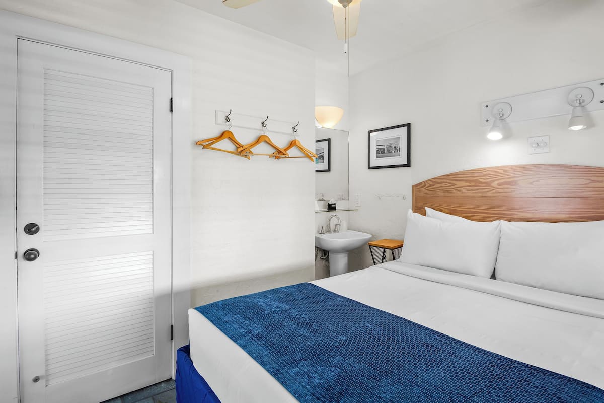 A hotel room with a large bed, a wooden headboard, a white sink, and a mirror.