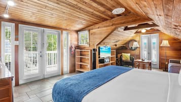 A cozy attic bedroom with a large bed, wooden ceiling, and a TV.