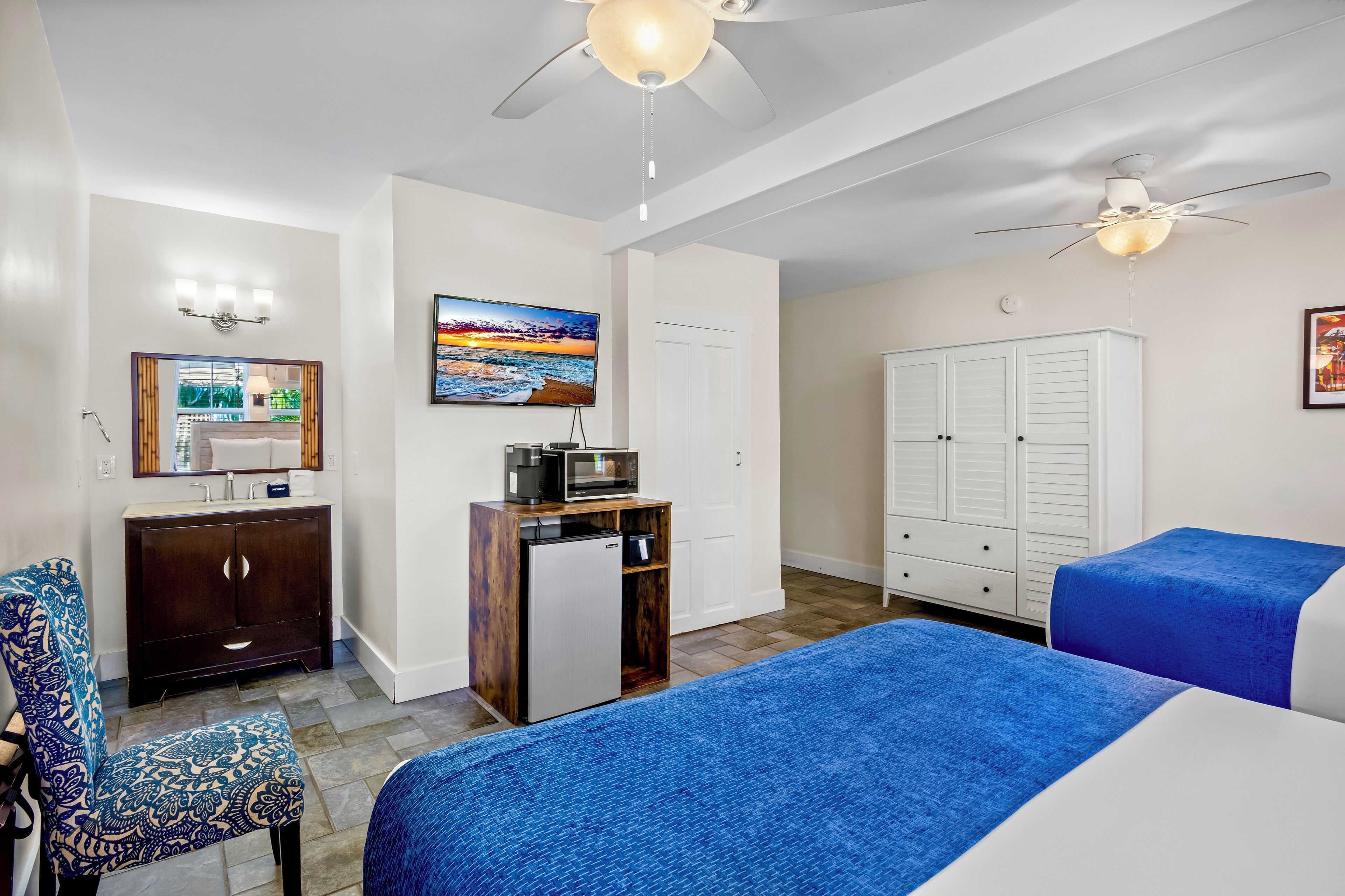 A hotel room with a bed, a desk, a chair, a wardrobe, and a ceiling fan.