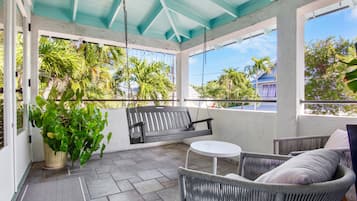 A covered patio area with a swing, wicker furniture, and a view of palm trees.