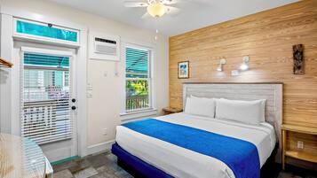 Ein Hotelzimmer mit Bett, Deckenventilator, Fenster mit Jalousien, einer Holzpaneelausstattung und einem kleinen Tisch.