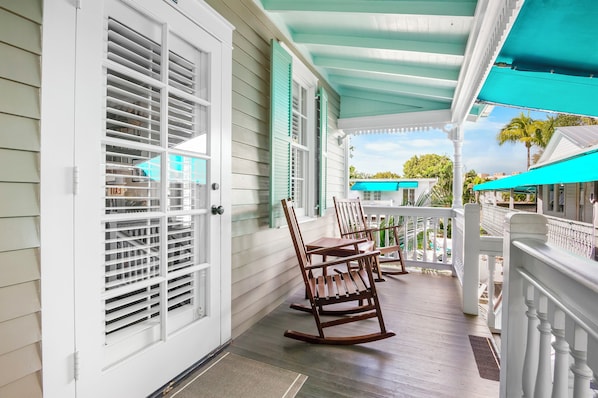 A porch with white railings, a rocking chair, and a covered area with a teal awning.