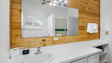 A modern bathroom with a wooden wall panel, a large mirror, a white sink, and a vanity with a towel rack.