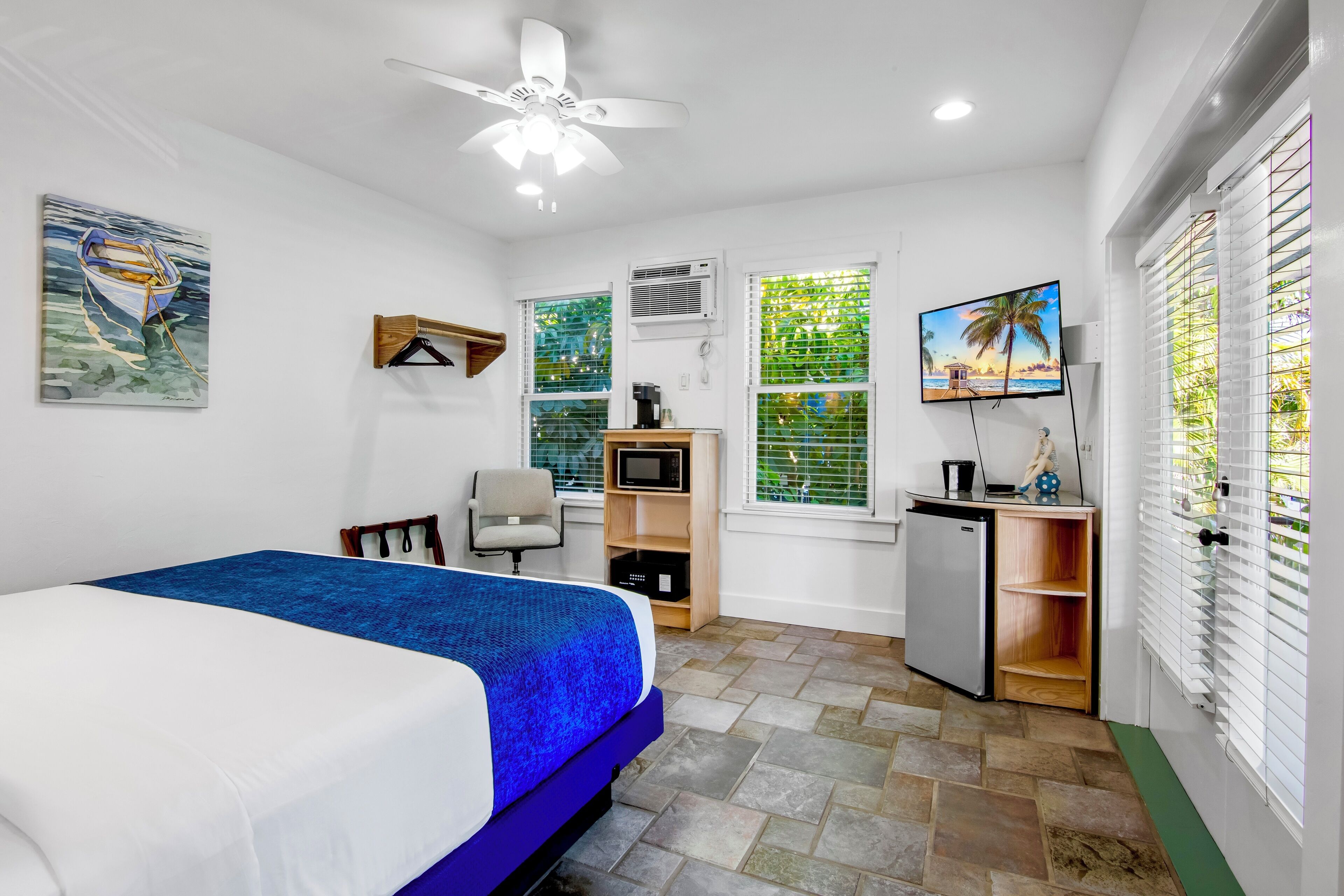 A bedroom with a bed, a desk, a chair, a TV, and a ceiling fan.