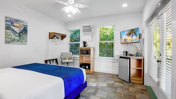 A bedroom with a bed, a desk, a chair, a TV, and a ceiling fan.