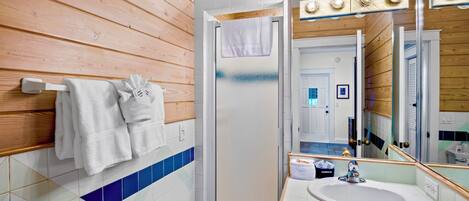 A bathroom with wooden panel walls, a tiled floor, a sink, a mirror with lights, and a shower.