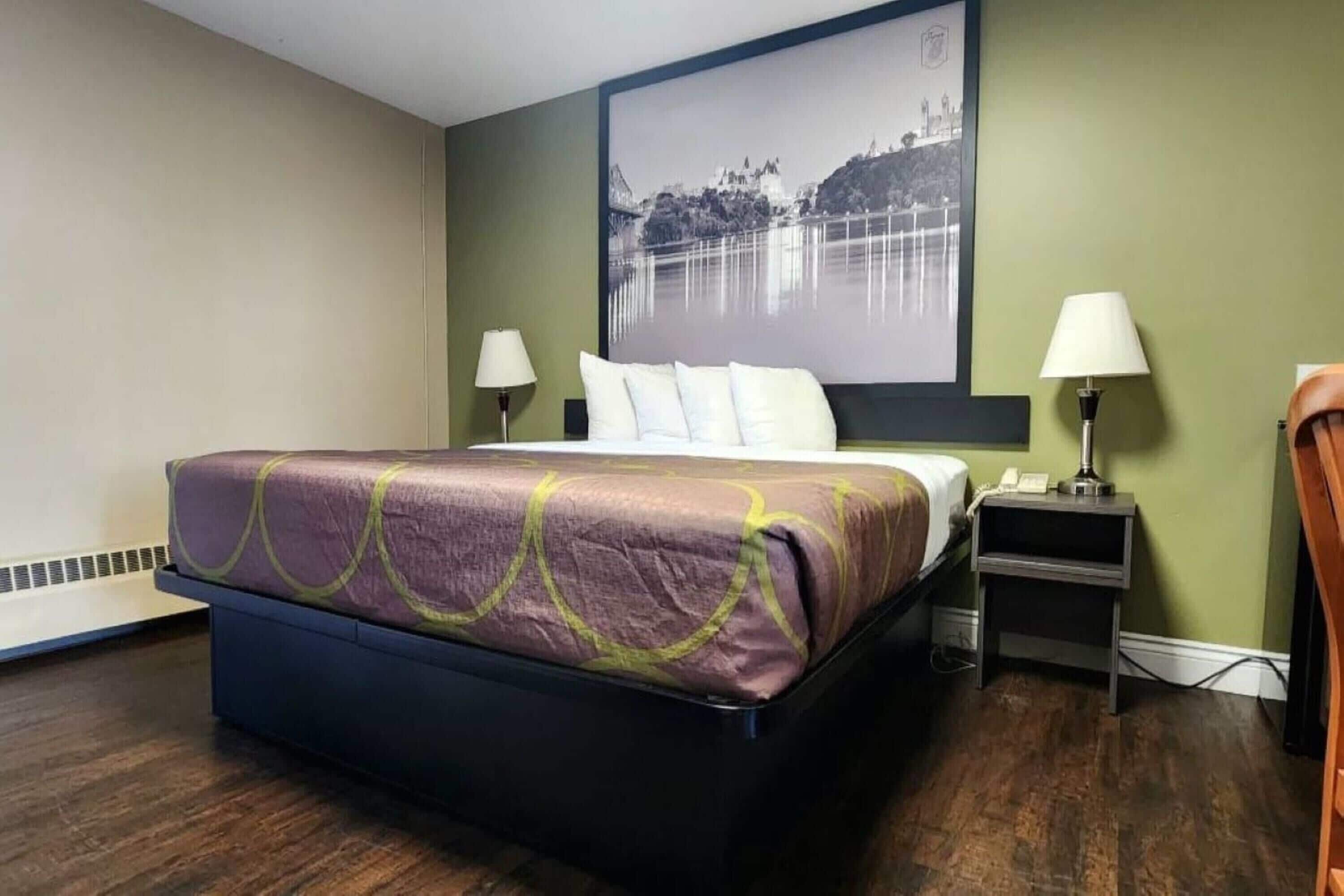 A hotel room with a bed, two bedside lamps, a nightstand, and a large framed picture on the wall.