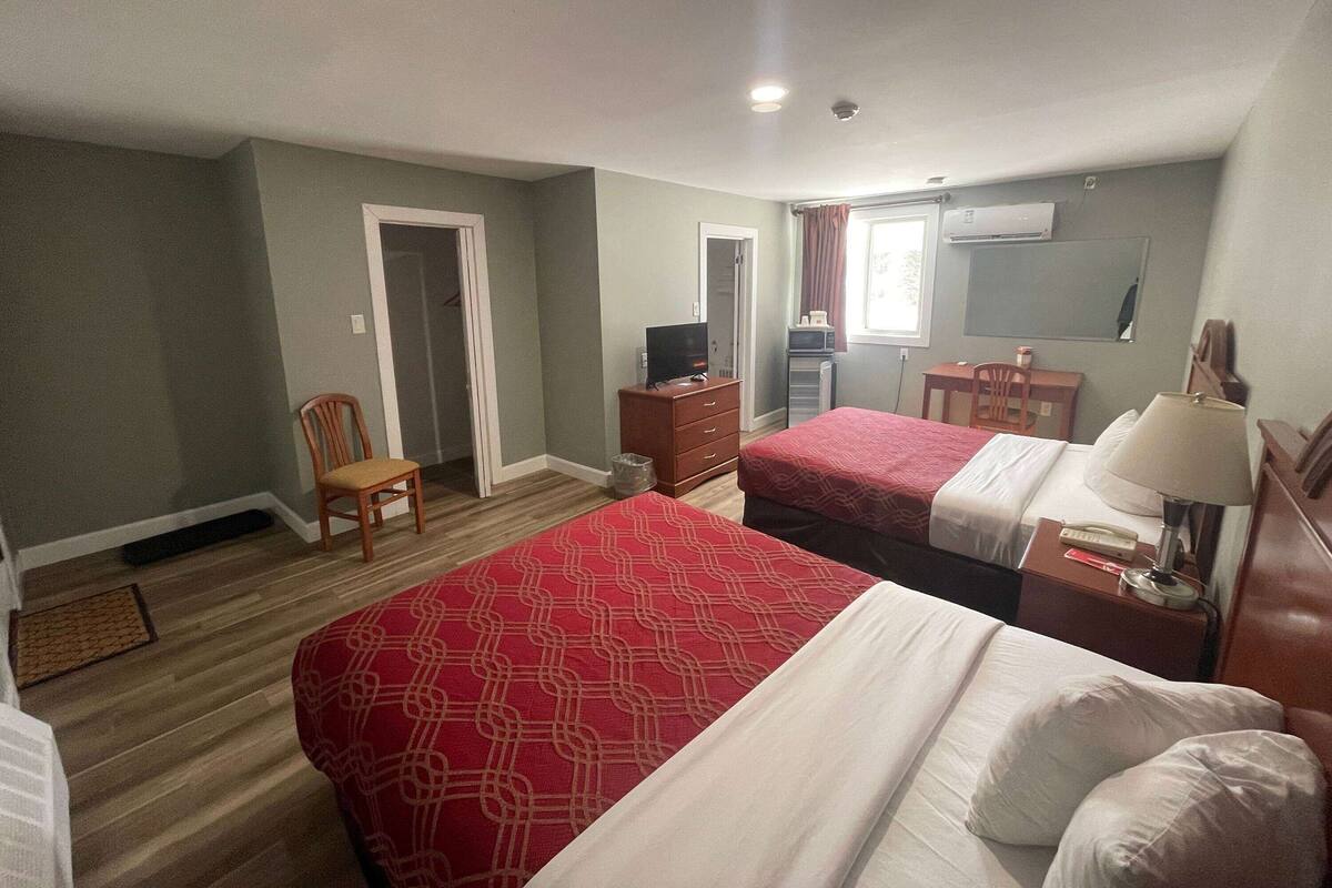 A hotel room with two beds, a desk, a chair, a TV, and an air conditioning unit.
