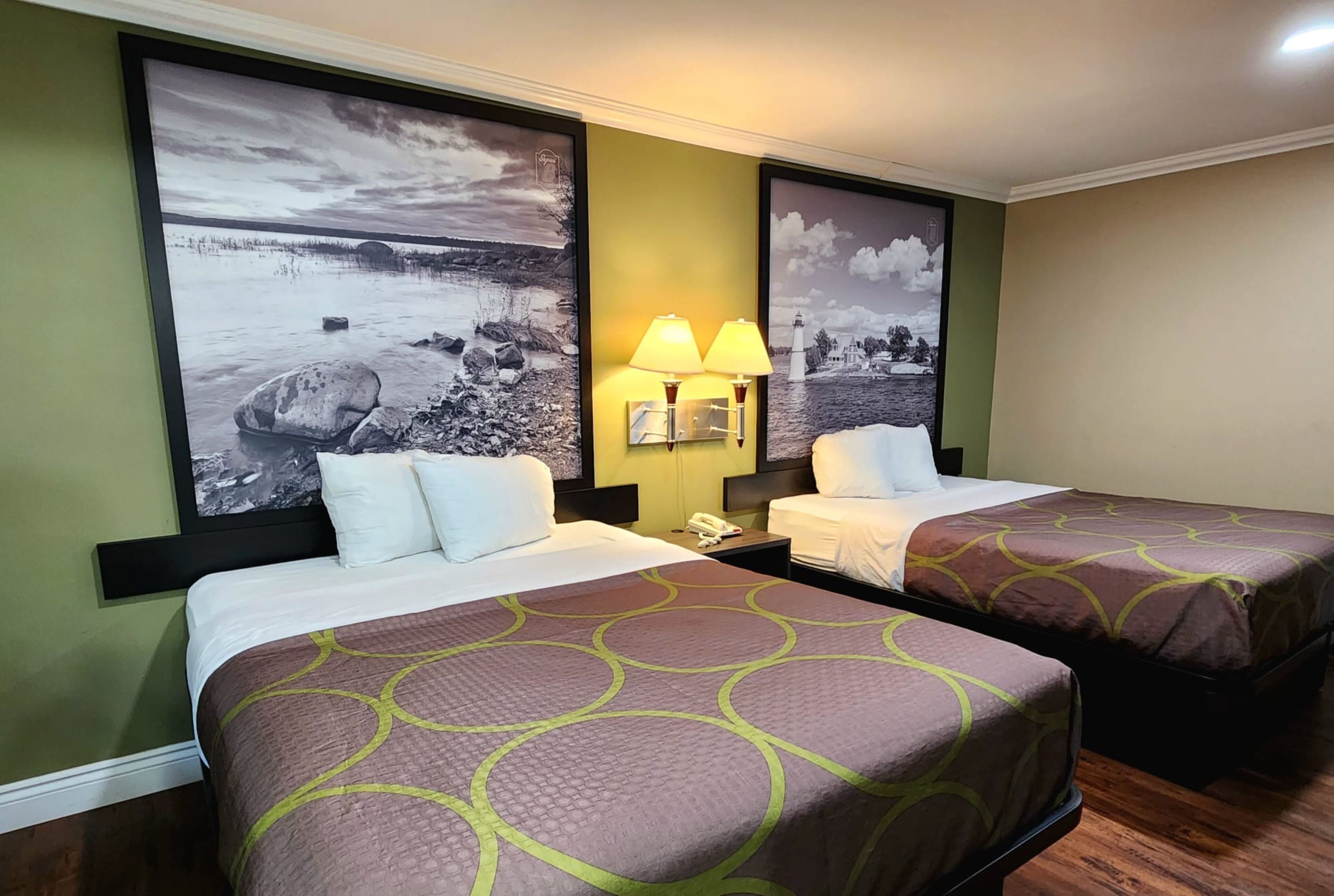 Habitación de hotel con dos camas, cada una con una colcha estampada, una mesita de noche con lámpara y grandes cuadros de paisajes en las paredes.