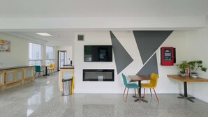 Un espacio de oficina moderno con una larga barra, varias sillas, una chimenea y un televisor montado en la pared.