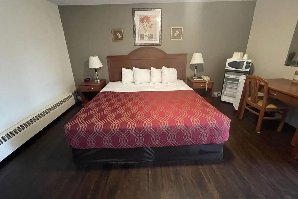 A hotel room with a large bed, a wooden desk, a microwave, a telephone, and a small table.