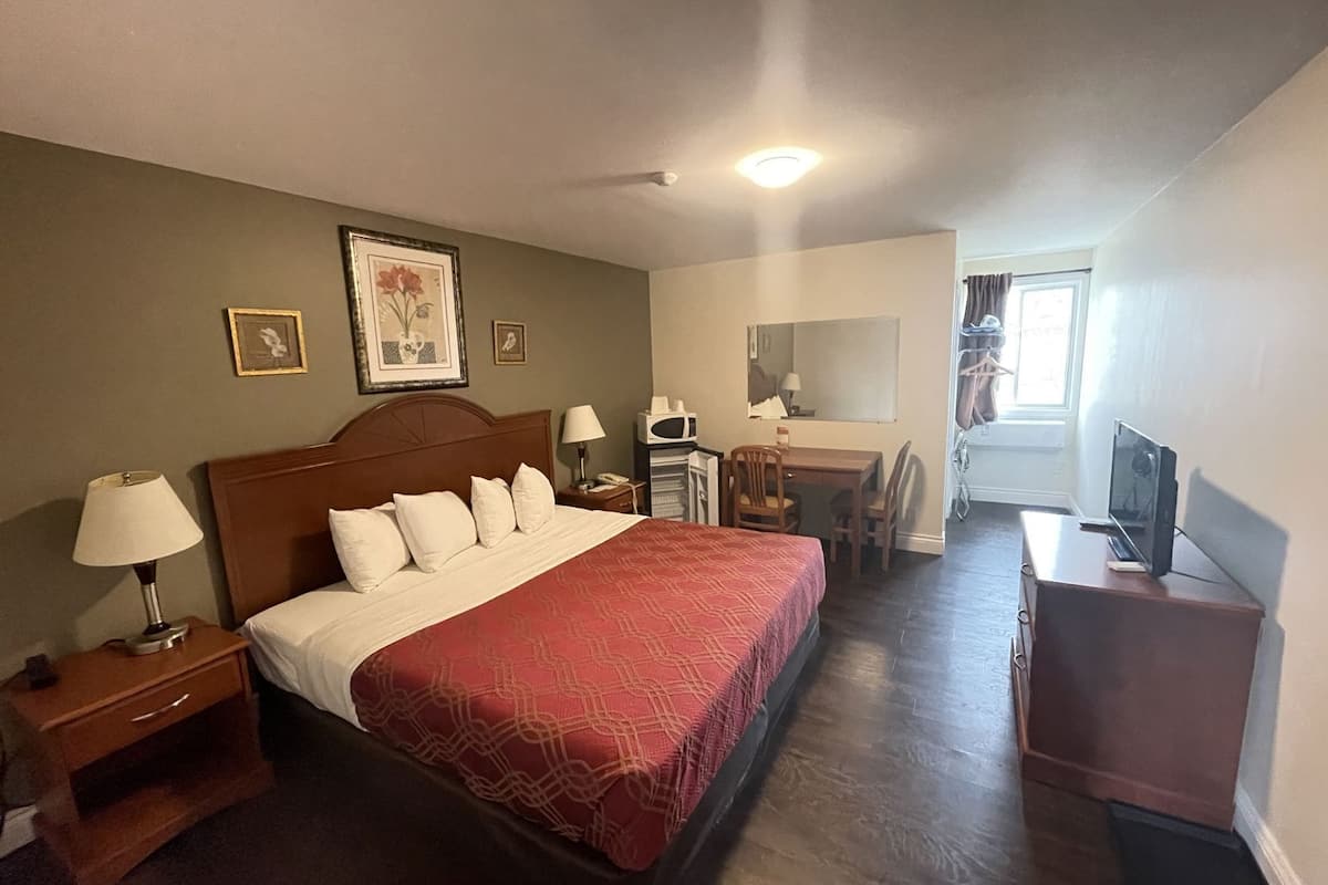 A hotel room with a bed, bedside tables, a desk, a chair, a television, and a window.