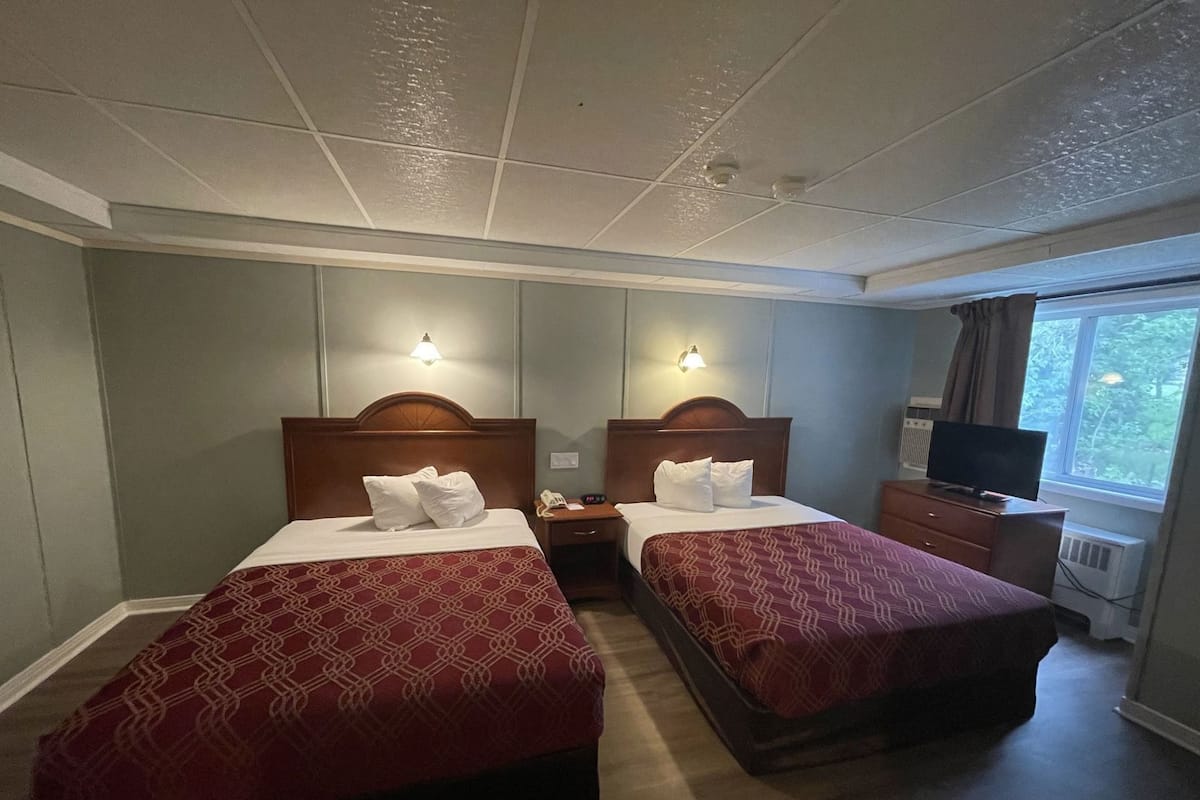 A hotel room with two beds, a television, a desk, and a window with a view.