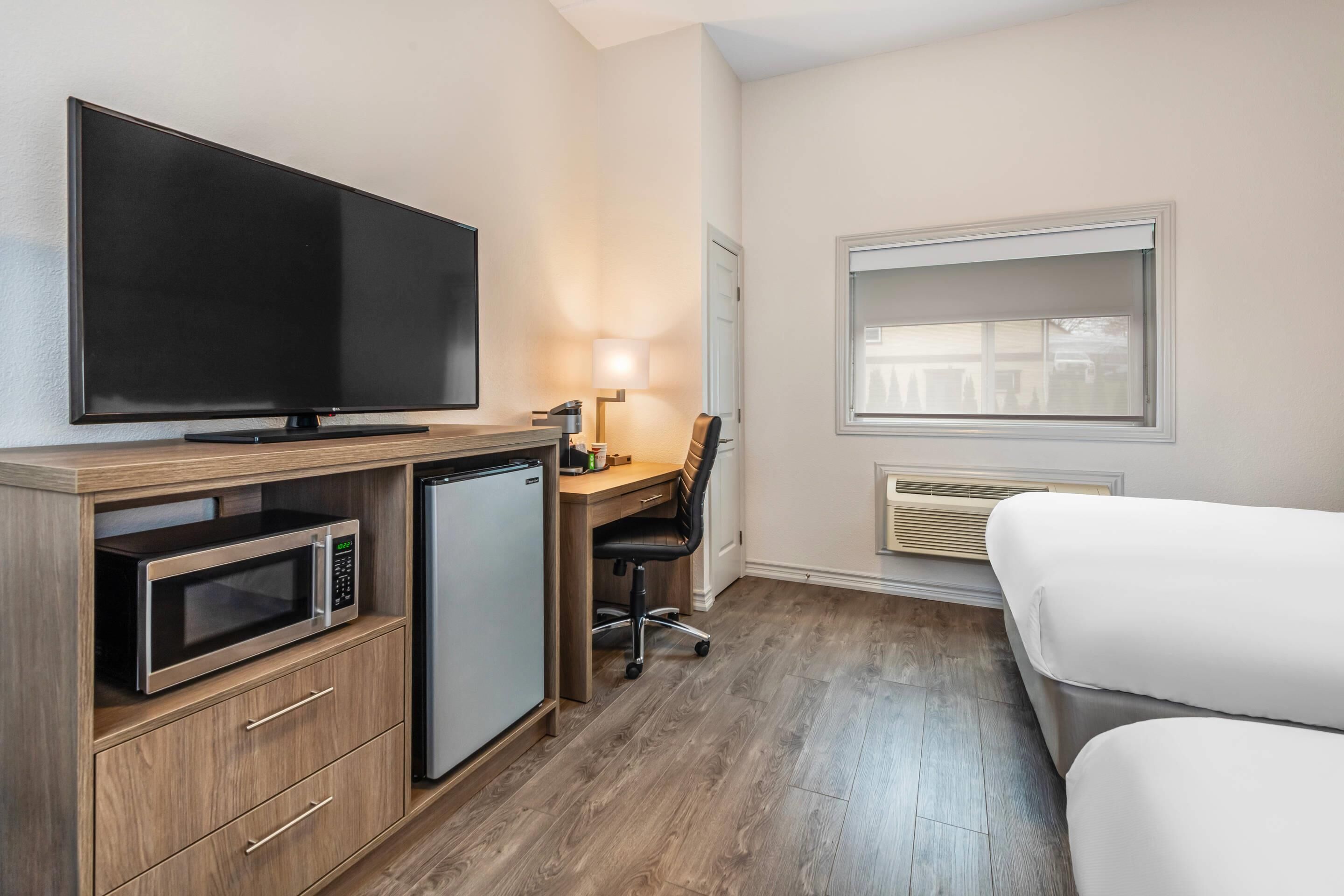 A hotel room with a flat-screen TV, a microwave, a mini-fridge, a desk with a chair, and a bed.