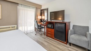Habitación de hotel con cama, escritorio con computadora, televisión, microondas y una silla.