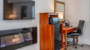 Habitación de hotel con televisión de pantalla plana, escritorio de madera con microondas, una silla y chimenea de diseño moderno.