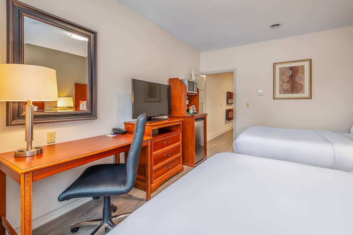 Une chambre d’hôtel équipée d’un bureau en bois, d’une chaise, d’un lit, d’une télévision et d’un four à micro-ondes.