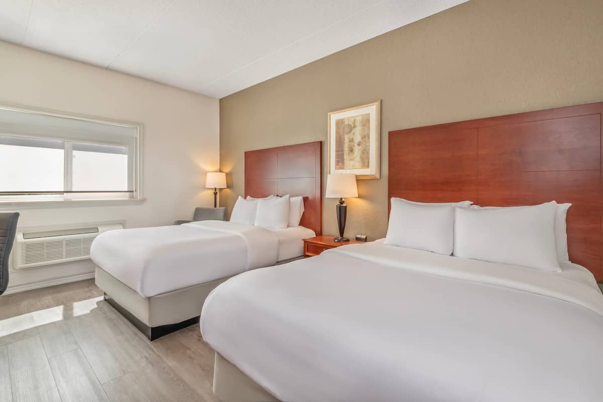 Een hotelkamer met twee bedden, een raam, een radiator en een schilderij aan de muur.