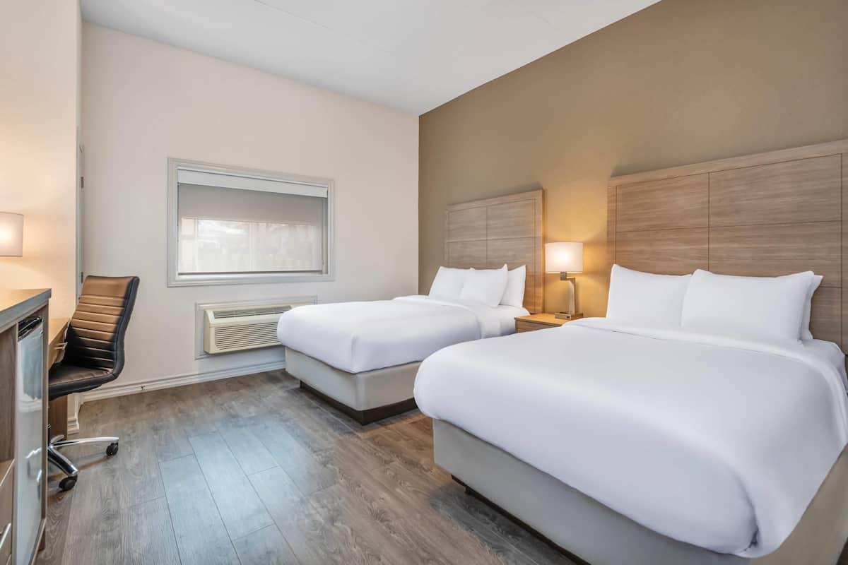 Een hotelkamer met twee bedden, een bureau, een stoel, een raam en een wandheater.