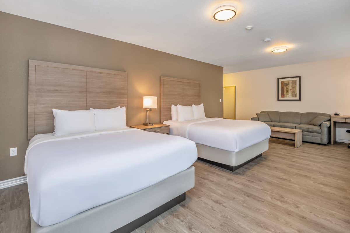 Een hotelkamer met twee bedden, een slaapbank, een bureau en een lamp.