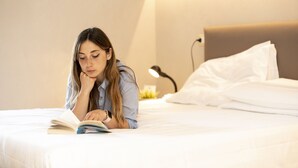 A person lying on a bed reading a book in a room with a bedside lamp and white bedding. - Hotel Ristorante Miranda (Riva di Solto)