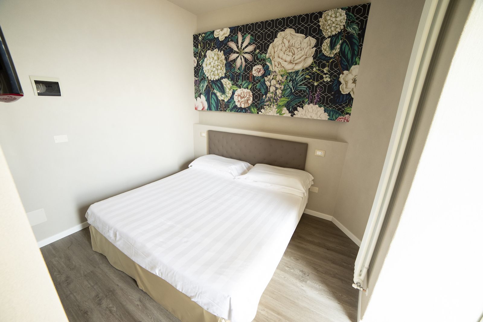 Quarto com cama, cabeceira, painel de parede floral e piso de madeira.