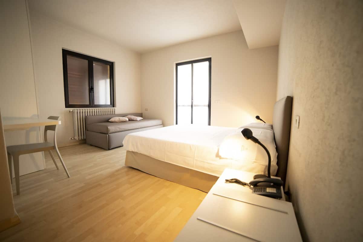 A modern bedroom with a bed, a desk, a chair, and a radiator.