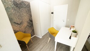 A small, modern room with a white door, a white table, and two chairs, one yellow and one gray. - Hotel Ristorante Miranda (Riva di Solto)