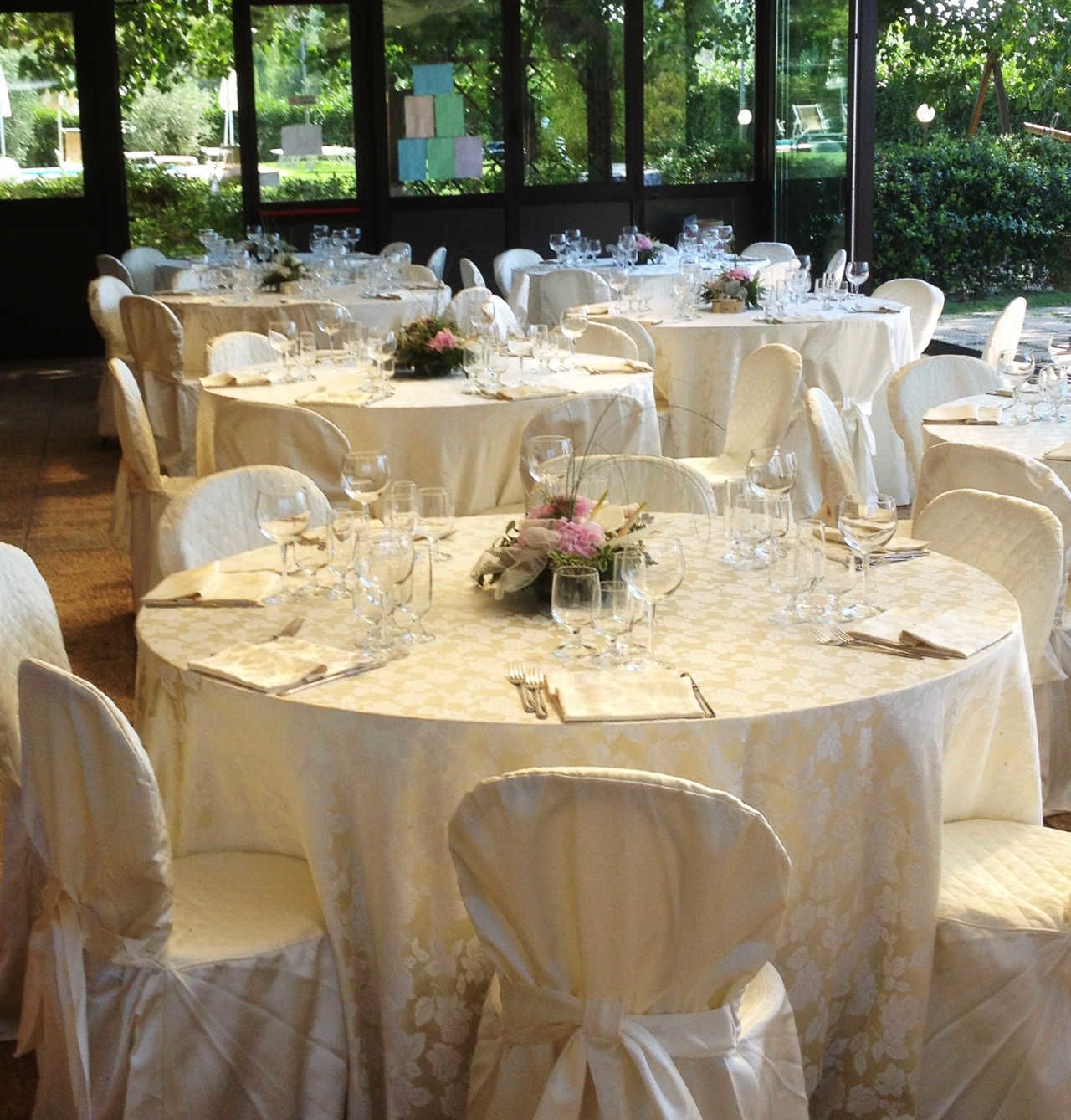 Een balzaal met ronde tafels gedekt voor een formeel evenement, elk met witte tafelkleden, glazen en bloemdecoraties.