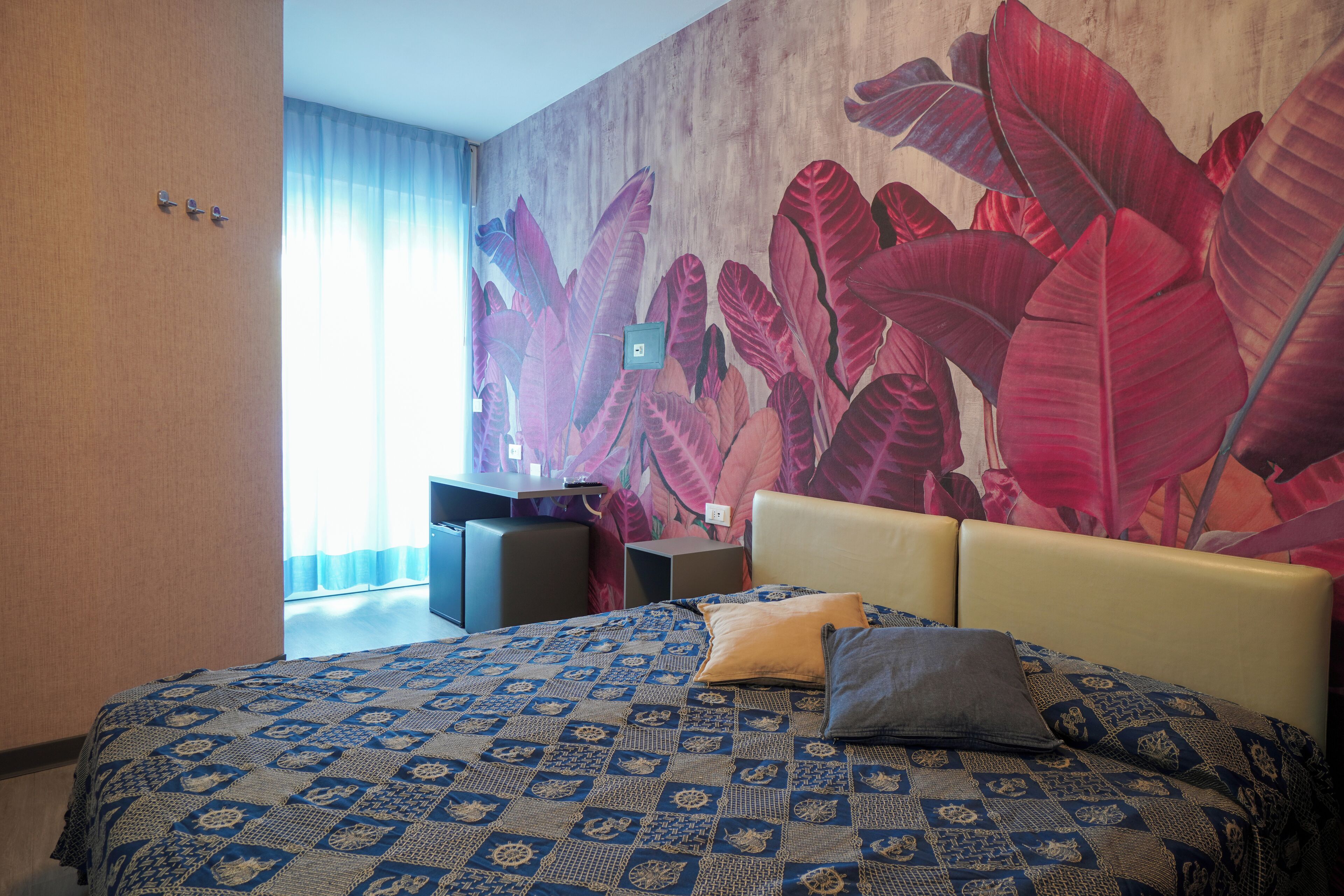 A hotel room with a large bed, a desk, and a wall mural.