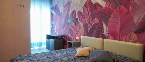 A hotel room with a large bed, a desk, and a wall mural.