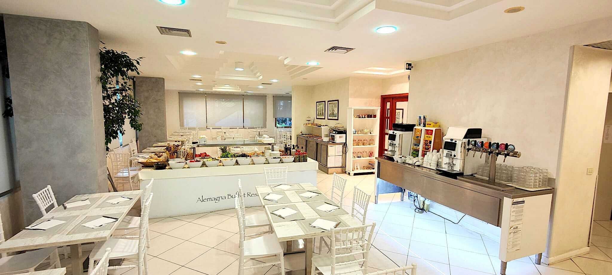 Un restaurant avec des tables et des chaises blanches, un buffet et une machine à café.