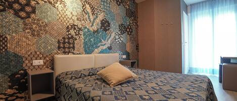 Una habitación de hotel con un papel tapiz estampado, una cama con colcha estampada, una mesita de noche y un escritorio.