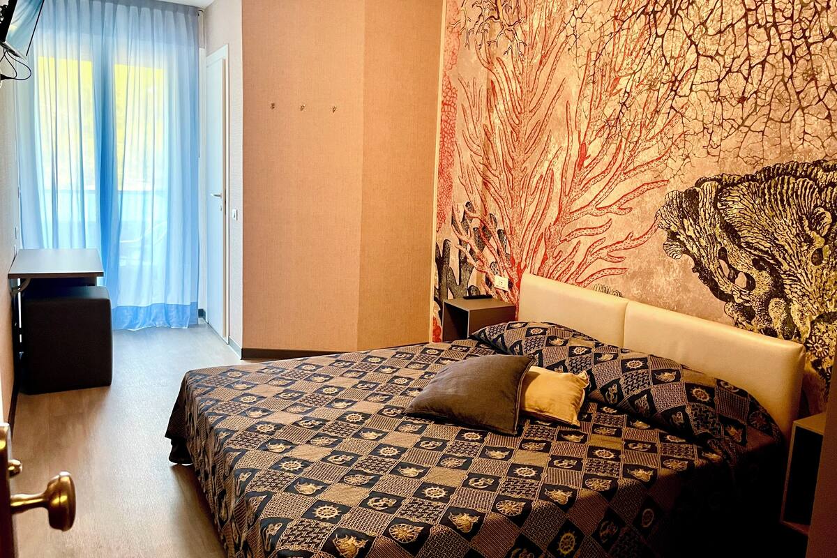 Een hotelkamer met een bed, een televisie, een bureau en een groot wandtapijt.