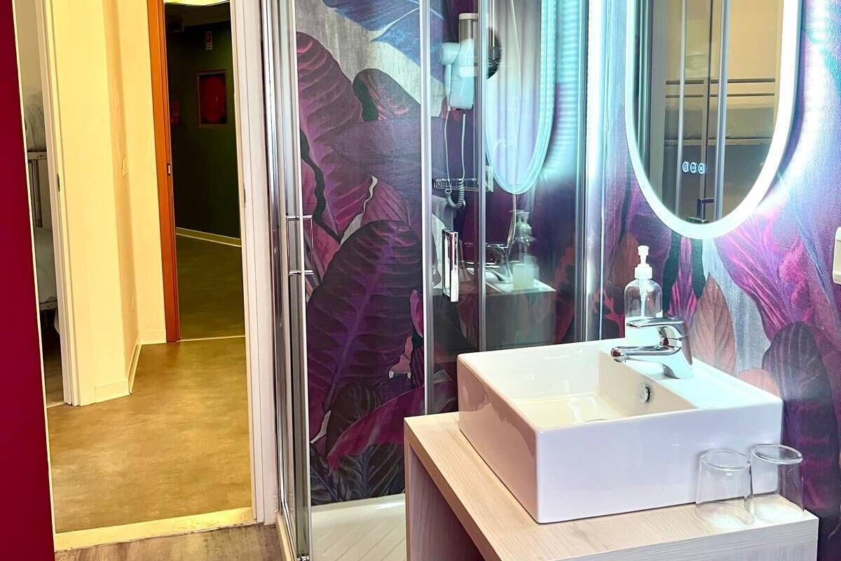 Een moderne badkamer met een douchecabine van glas, een wastafel met spiegel en een grote spiegel met verlichting.