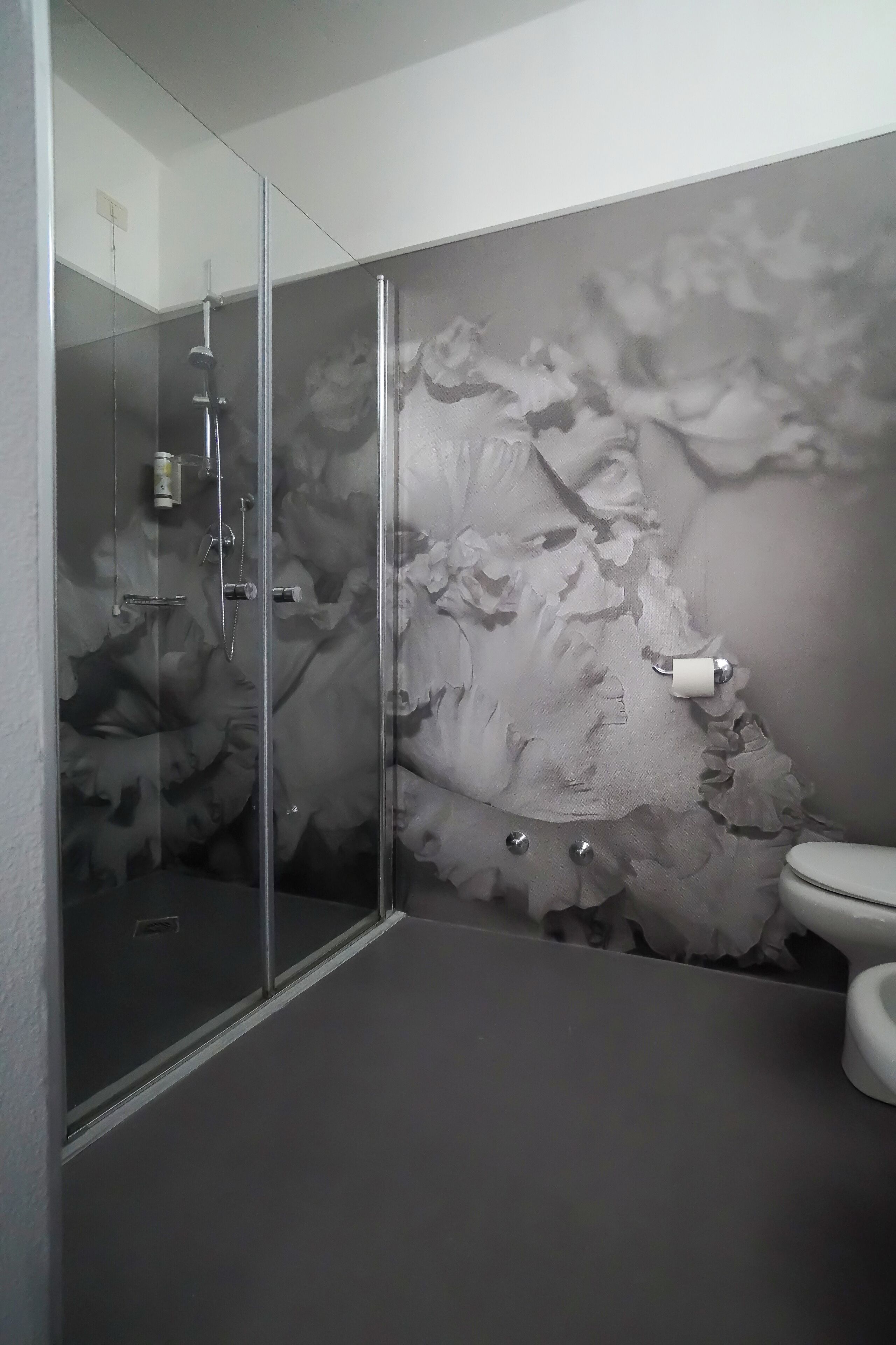 Un baño moderno con cabina de ducha de vidrio, inodoro y un mural floral decorativo.