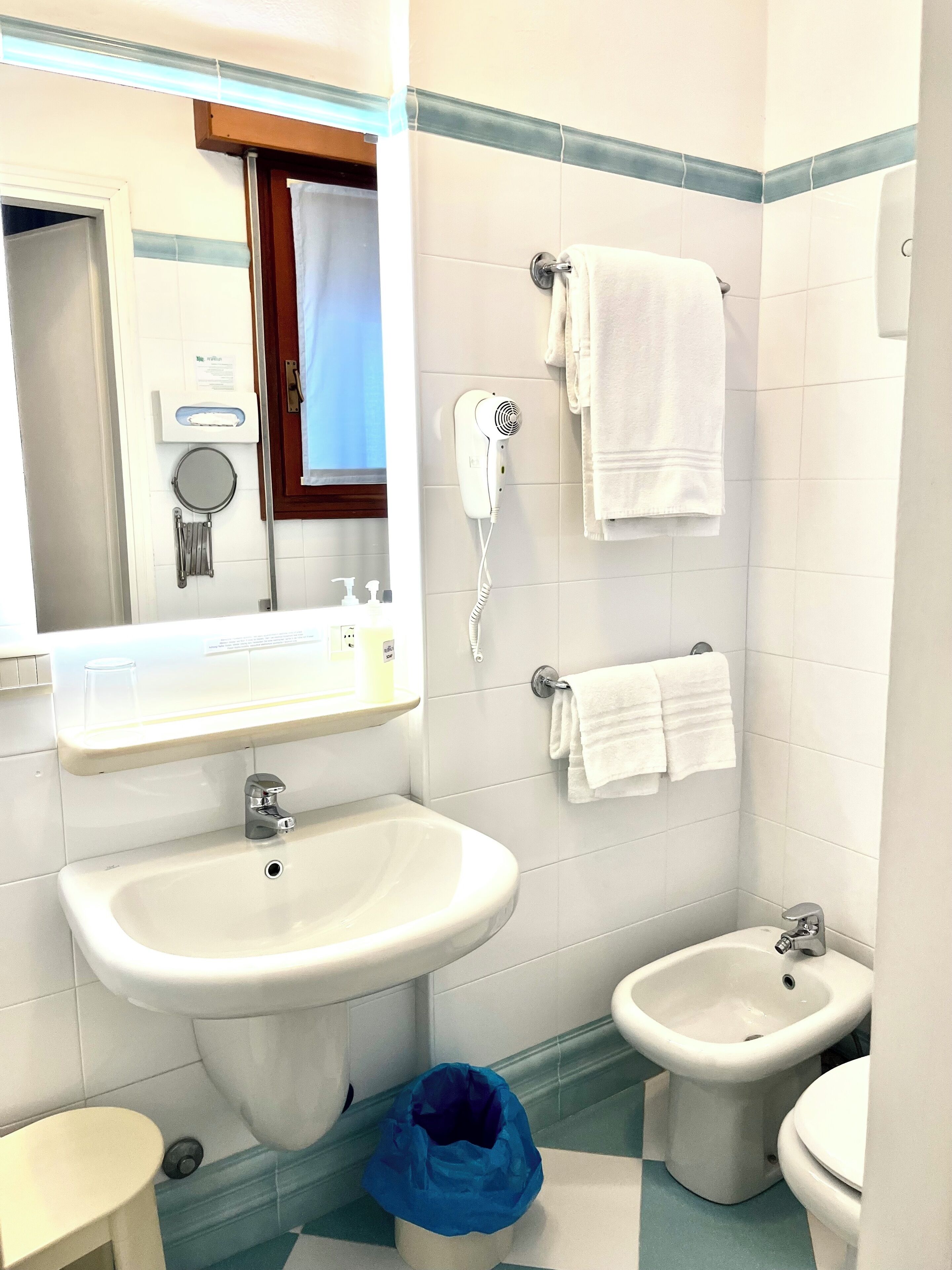 Un bagno con lavandino, bidet e asciugacapelli fissato alla parete.