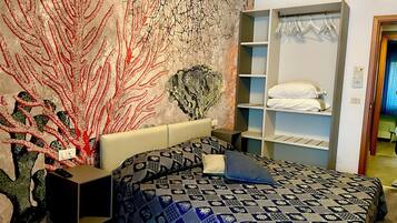 A bedroom with a patterned bedspread, a wall mural, a built-in wardrobe, and a bedside table with a remote control.