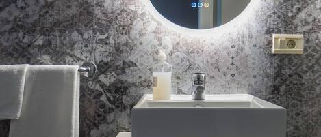 A bathroom with a white sink, a round mirror, and a towel hanging on a rack.