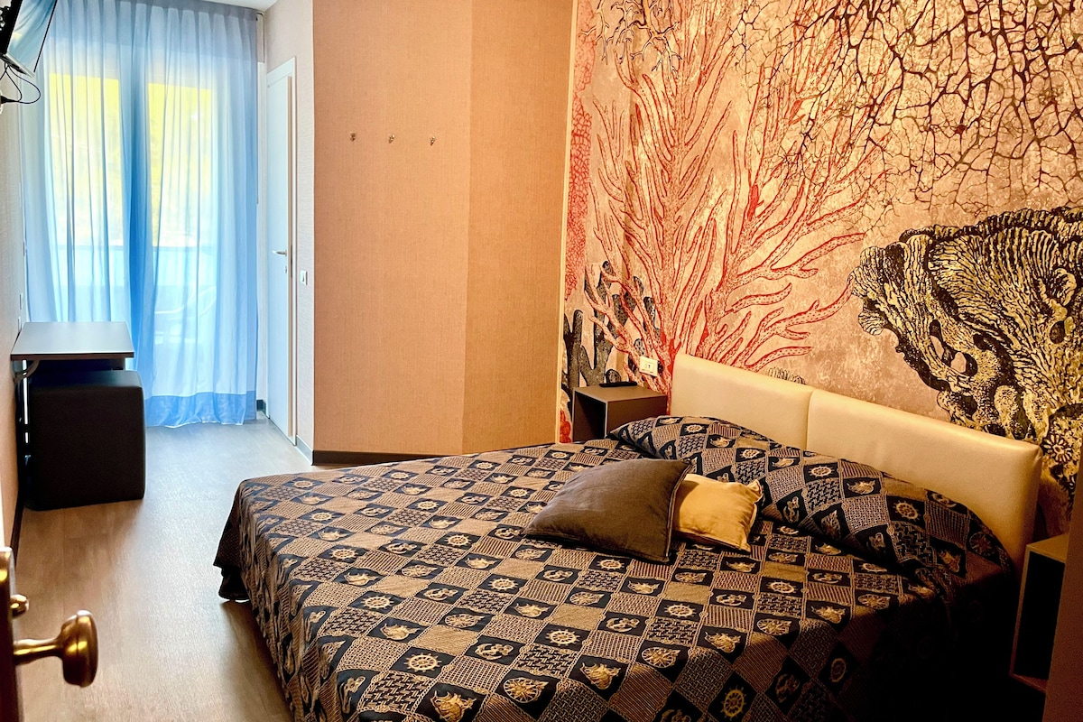 Une chambre d’hôtel avec un lit, une télévision, un bureau et une grande tapisserie au mur.