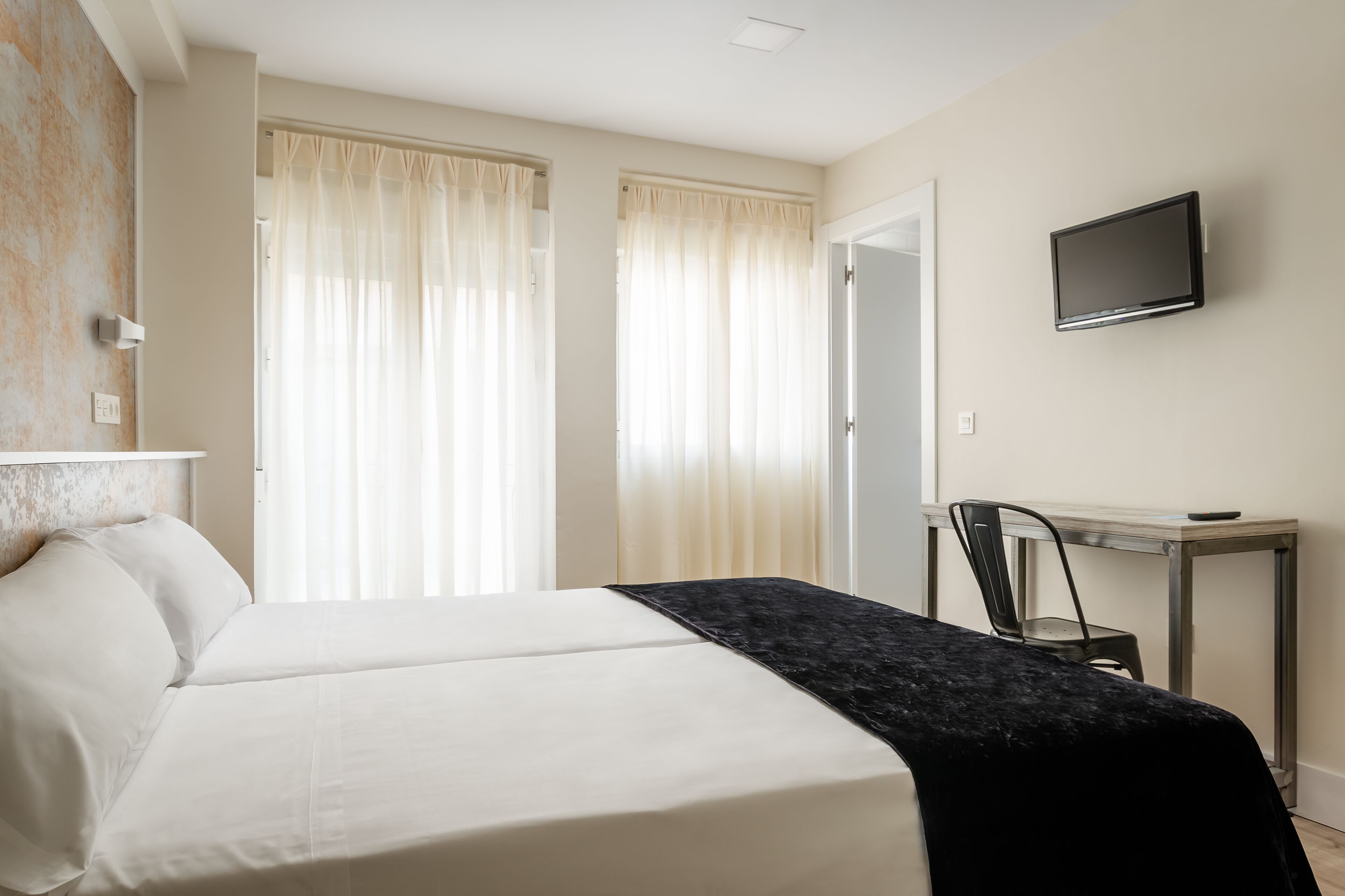 Une chambre d’hôtel avec un lit, un bureau, une chaise et un téléviseur.