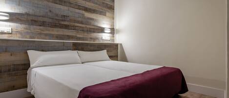 Un dormitorio con cabecera de madera, cubrecama blanco y manta roja.
