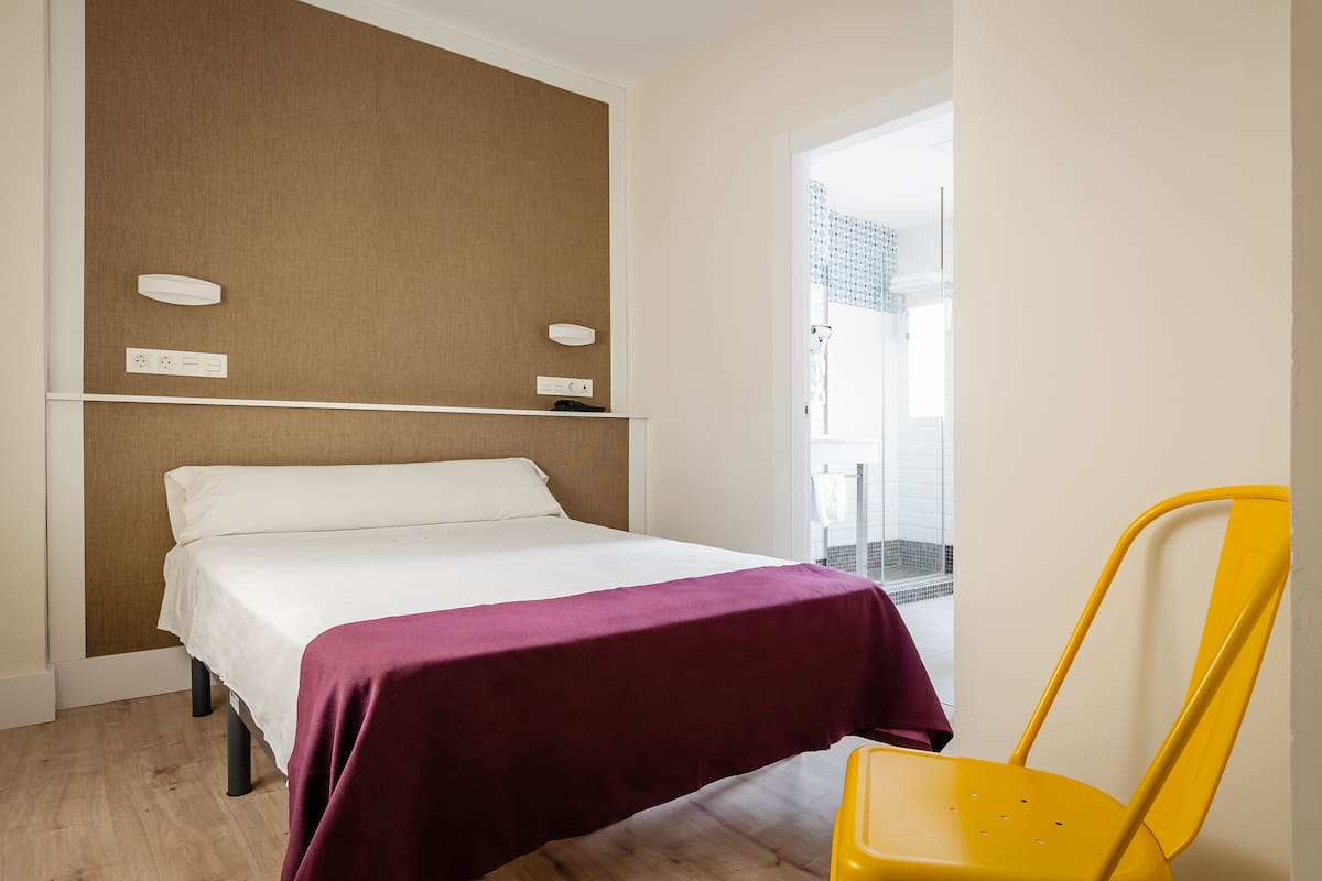 Una habitación de hotel con una cama, una silla amarilla y vista a una zona con baldosas.