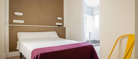 A hotel room with a bed, a yellow chair, and a view of a tiled area.