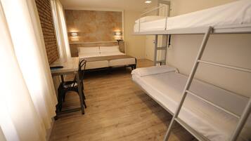 A bunk bed room with a desk and chair, wooden flooring, and a brick wall.