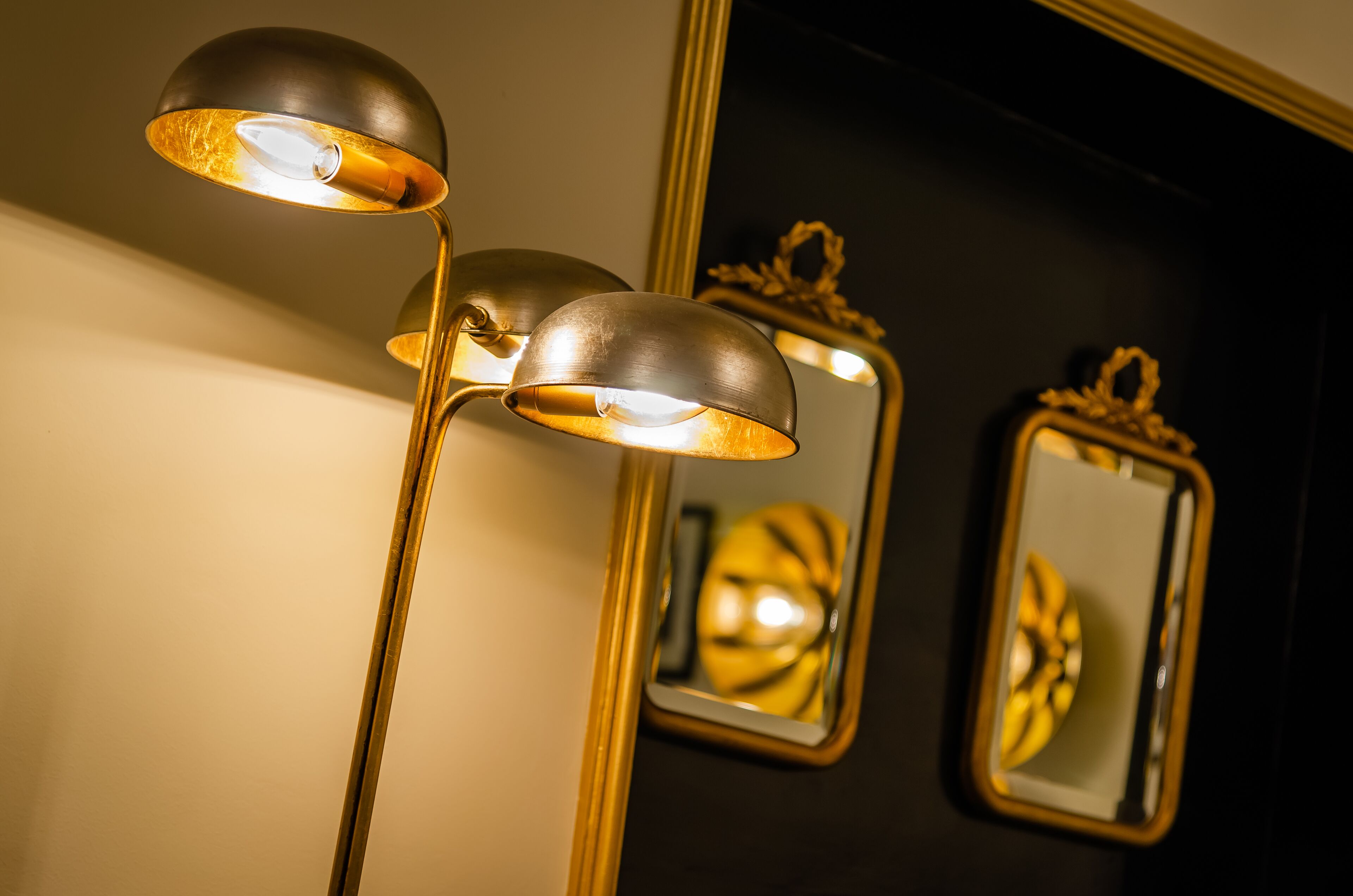 A floor lamp with three shades and a mirror reflecting its light.