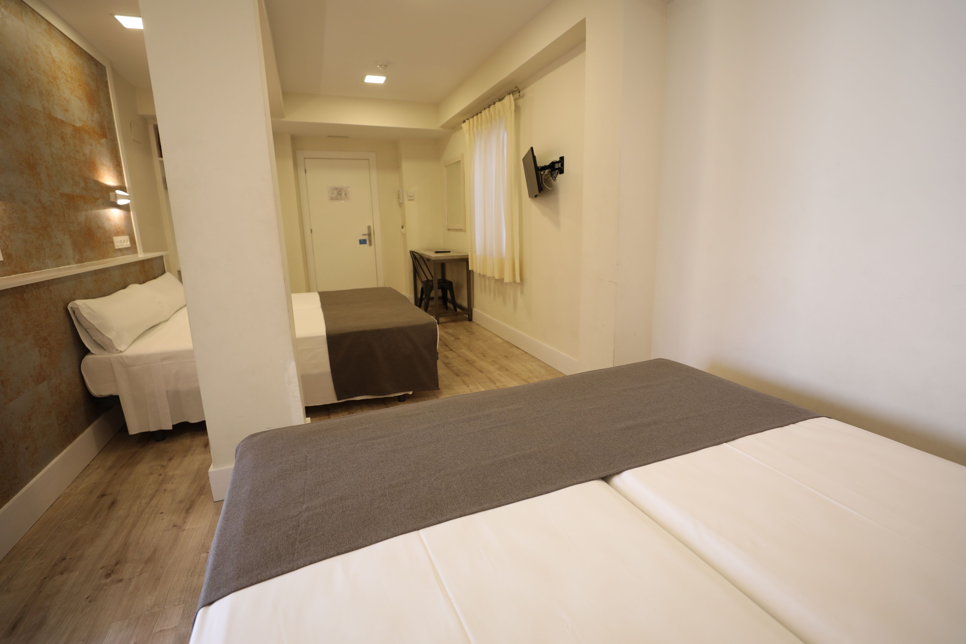 A hotel room with a bed, a small desk, a chair, and a TV mounted on the wall.