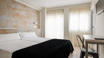 A hotel room with a large bed, a desk, and a chair.