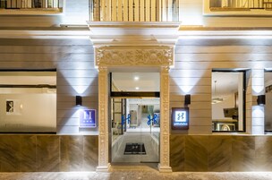 Entrada de hotel con un arco imponente, puertas de cristal y una recepción a la vista.